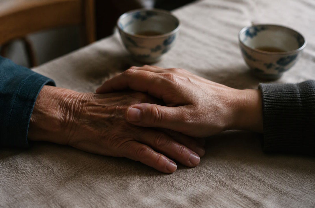 Une main âgée et une main plus jeune posées l'une sur l'autre sur une nappe en lin